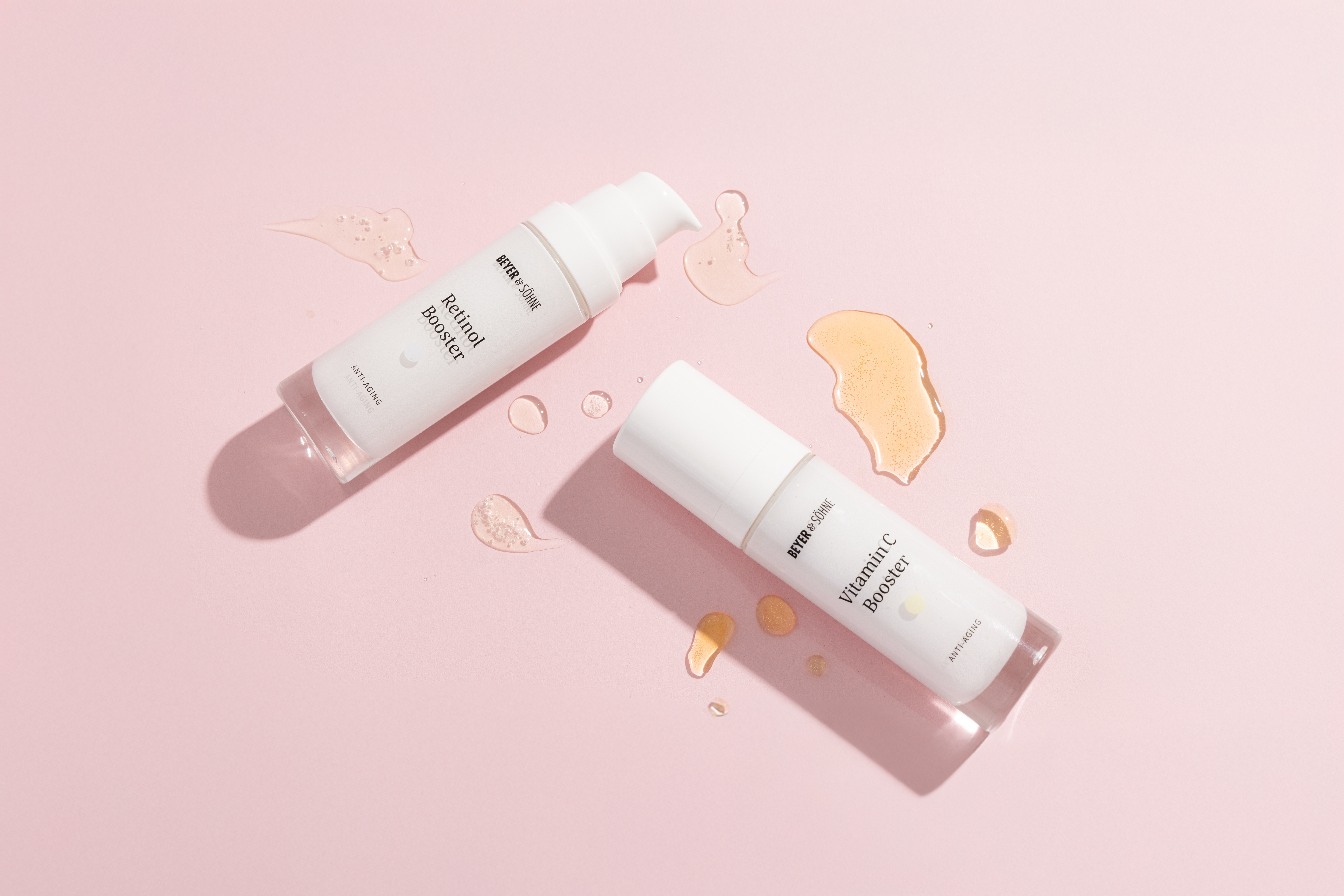 Beyer & Söhne Retinol und Vitamin C Booster Spender auf rosa Hintergrund mit transparenten Gel-Texturen beider Produkte